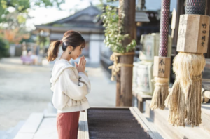 神社で手を合わせてお祈りをする女性